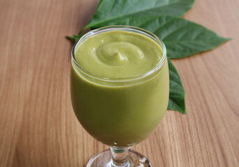 Rich, finely blended green avocado pulp in a stemmed glass sits on the table next to the green leaves.

