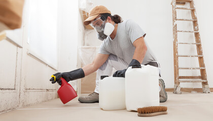 In the home renovation site worker using products for mold remediation treatment wearing a respirator mask and using bottle spray. Concept of house painting, cleaning and mold removal service