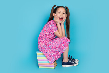 Fototapeta premium Full length photo of excited attractive little lady dressed pink outfit sitting book pile empty space isolated blue color background