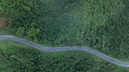 Aerial view from above of country road through the green summer forest in summer Thailand. Top view of the asphalt road and dense green forests.