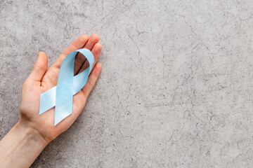 Blue ribbon symbol of colon or prostate cancer with hands. Medical support and prevention