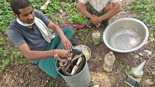 A Indian beekeeper extracting  honey with a honey extractor. Beekeeper inspecting his honey bees and honeycomb carefully in the sunlight. Indian Beekeeping. Honey production
