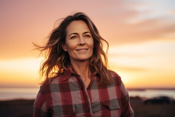 Portrait of a smiling woman in her 40s dressed in a relaxed flannel shirt in vibrant sunset horizon