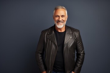 Portrait of a happy man in his 50s sporting a classic leather jacket while standing against modern...