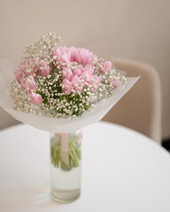 Wedding bouquet of pink tulips and white gypsophila flowers in gift paper in vase on table. Alpine gypsophila and Salmon Impression tulip. Gift flowers in bright room or cafe. Floristics concept.