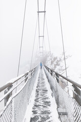 Suspension bridge in a snowstorm. Pedestrian crosses narrow suspension bridge in the fog....