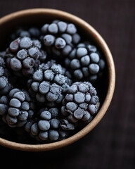 Frozen blackberries. Ceramic bowl with frozen forest berries. Cold blackberries in frost. refreshing dessert. Healthy food. Black background. Top view. Close-up. Soft focus. High quality photo