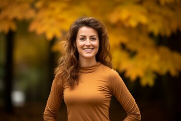 Portrait of a jovial woman in her 30s showing off a lightweight base layer isolated in background of autumn leaves