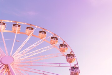 Fototapeta premium A vibrant and colorful Ferris wheel set against the backdrop of a beautiful sunset at the fairground. Light purple pink lavender sky.