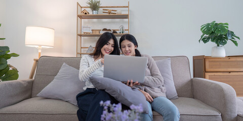 Lesbian Couple Enjoying a Video Call on Laptop While Sitting on a Cozy Sofa in a Modern Living Room