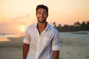 Portrait of a cheerful indian man in his 20s wearing a simple cotton shirt isolated in beautiful beach sunset