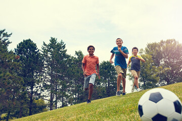 Naklejka premium Soccer, running and boy children in park for bonding, games and fun outdoor holiday together. Sports, kids and happy friends playing on grass with smile, ball and energy on summer camp for football.