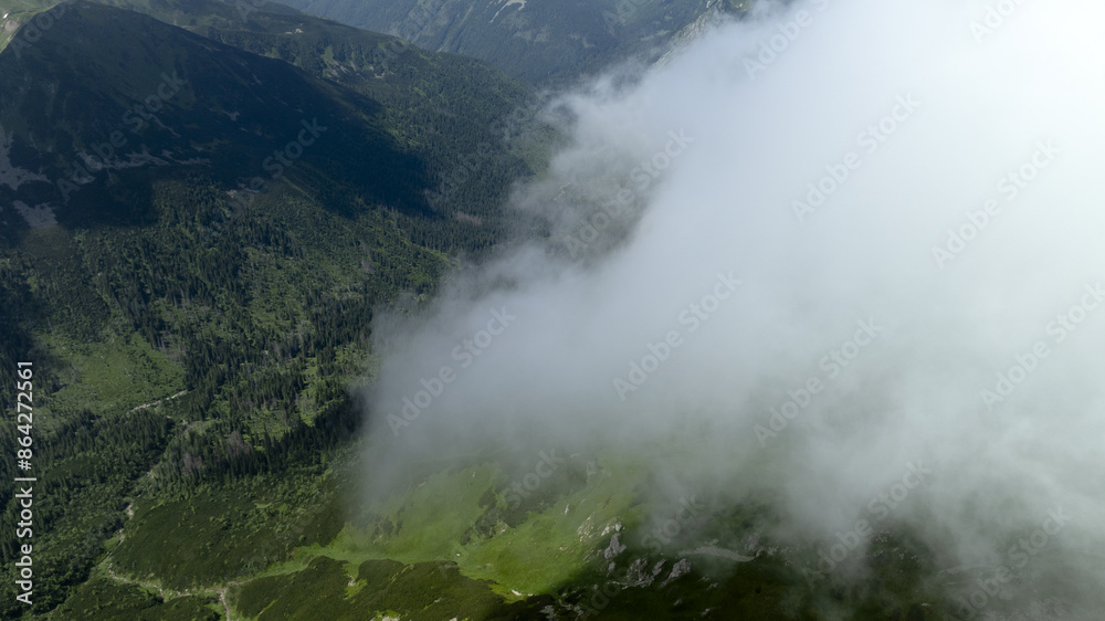 Sticker clouds veil the terrain below, trees line mountain sides