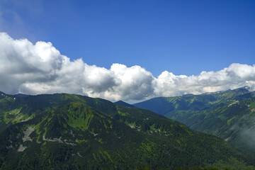 Naklejka premium green peaks in the foreground, blue sky with white clouds overhead