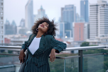 Obraz premium African businesswoman relaxes when she on the rooftop getting some fresh air after a tense meeting, tall building in the background