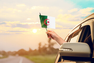 Waving the Algeria flag against the sunrise or sunset from a car driving along a country road....