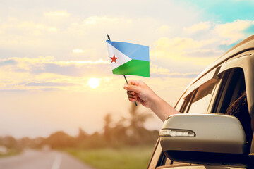 Waving the Djibouti flag against the sunrise or sunset from a car driving along a country road. Holding the Djibouti flag, traveling by car, on a weekend trip.