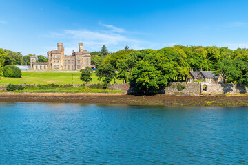 The historic Lews Castle and a small stone cottage  along the harbor port of the village of Stornoway, Scotland, on Lewis and Harris Island in the Outer Hebrides. © Kirk Fisher