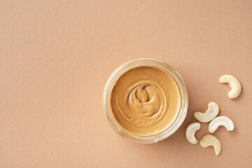 Nutritious cashew butter in glass jar and heap of nuts on table top view.