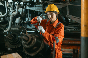 woman in a yellow helmet and orange work clothes is working on a machine