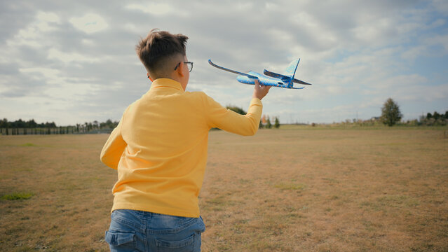 Back view happy Caucasian teen little boy child kid adopted son schoolboy enjoying summer holidays playing launching plane toy airplane flight dreaming to become a pilot travelling nature field meadow - Powered by Adobe