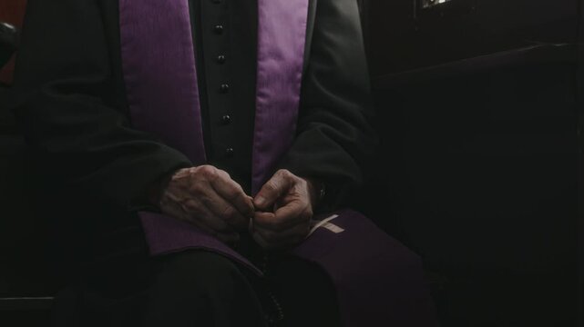Midsection shot of unrecognizable Catholic priest wearing cassock and purple stole sitting in confession booth