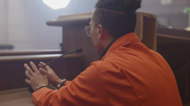 Zoom out from handcuffs to inmate testifying