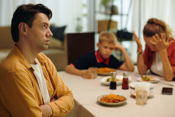 Man sitting at table with his family and looking tired of conflict with his wife
