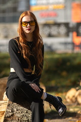 Portrait of a young beautiful red-haired girl in dark clothes outdoors.