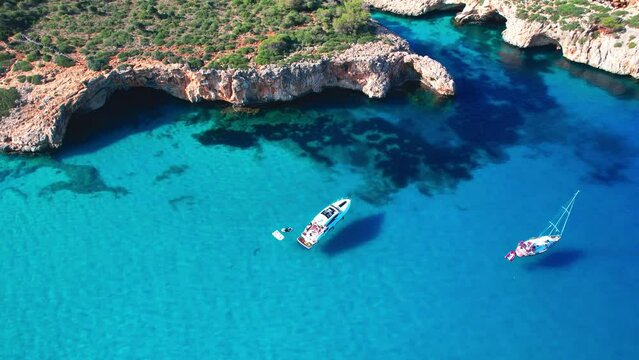4K Aerial Drone video of the most incredible turquoise blue water color with a unique rocky cliff formation and boats anchored in on a beautiful summer sunny day, Cala Varques secluded beach, Mallorca