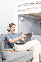 Young attractive woman in headphones listening to music during break of studying online at home. Distance education concept