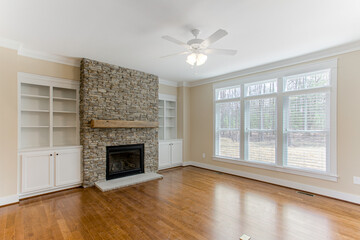 Spacious Living Room with Stone Fireplace and Large Windows Providing Light, Built in Shelves