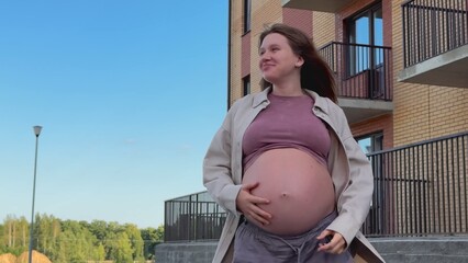 Young happy pregnant woman owner of new flat outdoors showing keys 