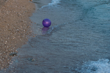 purple ball in the seashore in water with nobody around
