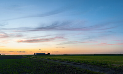 Naklejka premium Evening cirrus clouds above a farm in an empty rural landscape