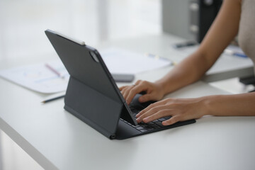 A person working on a tablet with a keyboard in an office setting, focusing on productivity and technology use. Modern workspace with natural light.