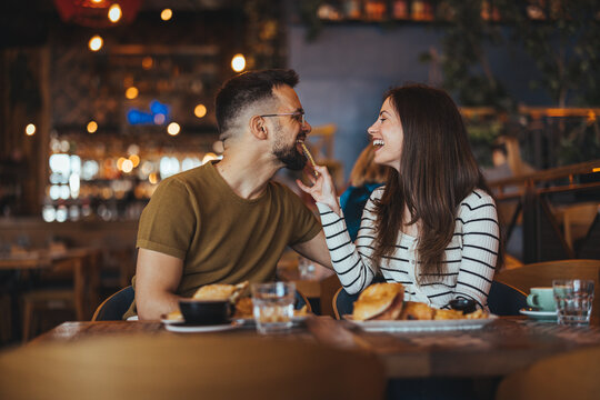 A joyful Caucasian couple engages in light conversation over a casual dining setup, with appetizing dishes enhancing their gastronomic experience in a dimly-lit restaurant.