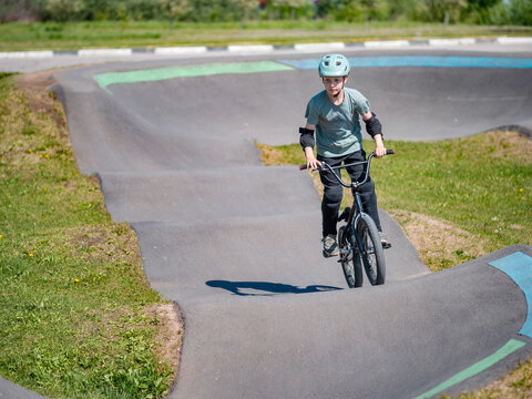 Child on bmx bike on pump track. Young male cyclist in helmet and protection rides bmx bike on asphalted bicycle race track. Boy BMX rider having fun and training on racing speed track. Extreme sport