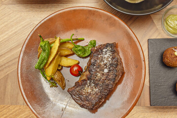 A piece of grilled meat with a side of French fries and roasted green peppers