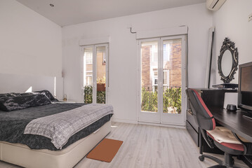 Bedroom with white furniture, white painted walls, two balconies with aluminum doors, flower pots, double bed and built-in wardrobe