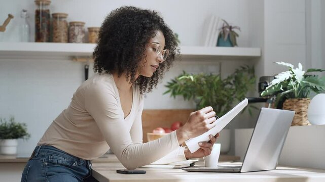 Video of cheerful attractive woman working with laptop in the kitchen at home.