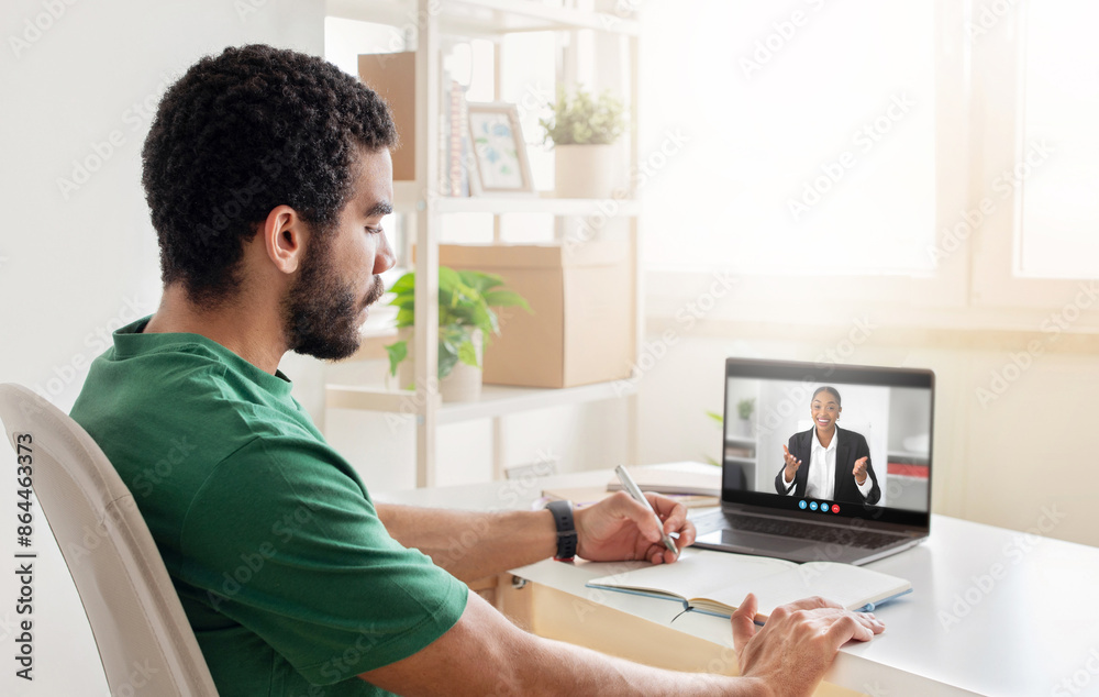 Aufkleber A man with a beard is seated at a desk and taking notes while listening to a woman on a video conference. He is wearing a green shirt and has a pen in his hand.