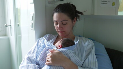 Mother’s hands carefully adjusting newborn baby’s clothing in a bassinet, viewed through crib...
