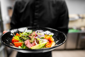Close-up of hands holding a colorful salad on a black plate