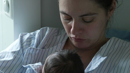 Mother Cradling Her Newborn Baby in a Hospital Room. The Baby, Wrapped in a Striped Shirt, Sleeps...