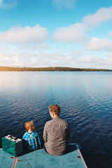 Fototapeta premium Back view, father and child by lake for fishing in summer for vacation, together and relax in morning. Family, fisherman and kid by water for holiday, learning or gear for outdoor adventure with dad