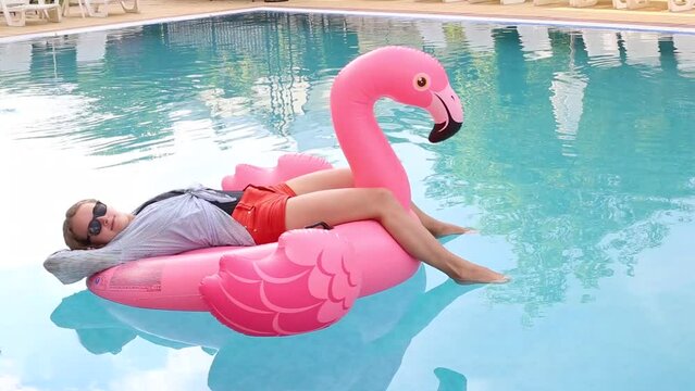 Woman on flamingo pool float  in pool in hotel. Summer holidays, enjoying summer vacations during quarantine. 
