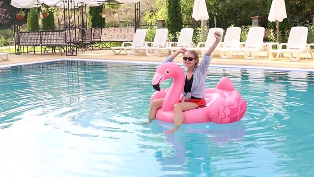 Woman on flamingo pool float  in pool in hotel. Summer holidays, enjoying summer vacations during quarantine. 
