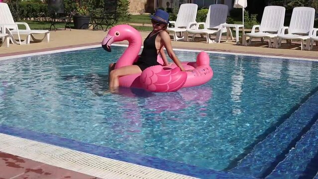 Summer holidays, relaxation. Woman on flamingo pool float and unicorn in pool. Enjoying summer vacations
