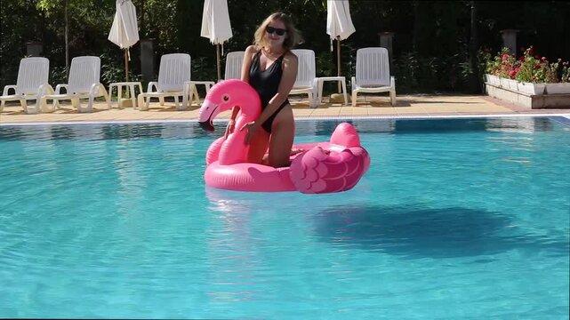 Beautiful woman on flamingo pool float and unicorn in pool. Summer holidays
